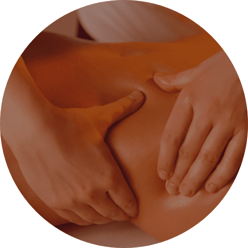 A close-up, circular image showing a person's hands massaging a lower back or hip area. The skin is light-colored, and the hands are gently kneading the area. The image is cropped in a circle with a gray background. The lighting is soft, highlighting the contours of the body and the hands. The focus is on the hands and the area being massaged.