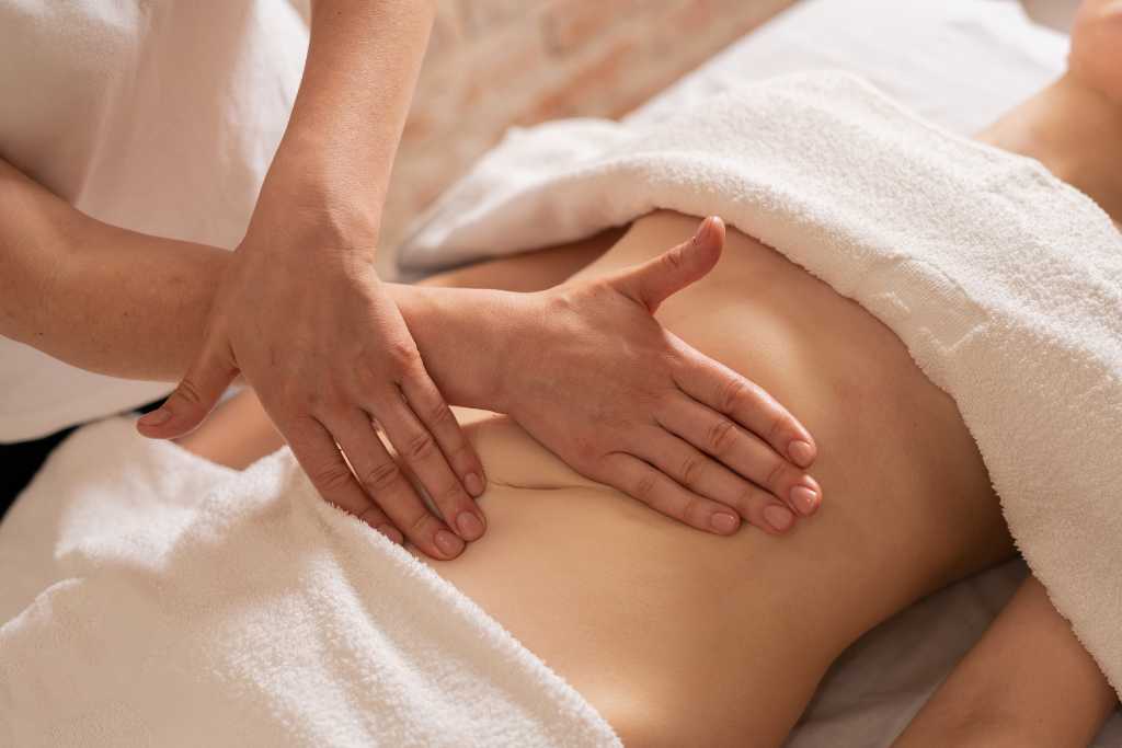Lymphatic drainage massage being performed on a person's stomach, with hands applying specific pressure.